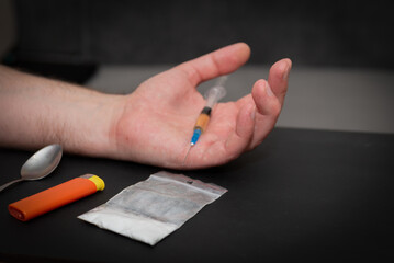 Drug Addict hand with syringe on dark room with a bag of drugs a spoon and a lighter.Toned.