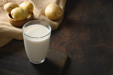 Vegan potato milk and potato on brown background. Close up. Copy space. Plant based milk replacer...