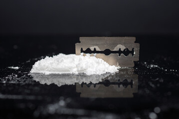 Razor Blade on drug powder on reflection black background.Copy space.