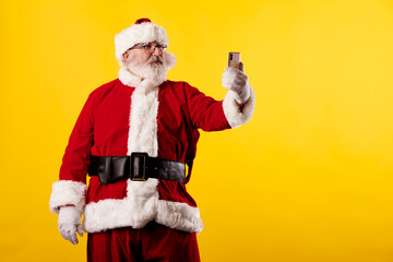 Fototapeta na wymiar Santa Claus taking a selfie with a mobile phone on a yellow background