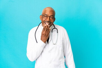 Senior doctor man isolated on blue background happy and smiling covering mouth with hand