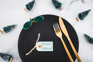 plant-based label on top of black dining plate with Christmas decorations all around on marble...