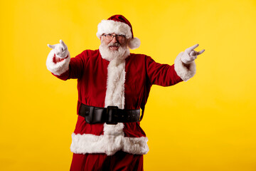 Fototapeta na wymiar Santa Claus making a rocker gesture on yellow background