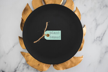 plant-based label on top of black dining plate with golden leaf decoration on marble table, healthy...