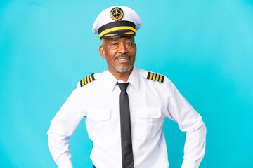 Airplane pilot senior man isolated on blue background posing with arms at hip and smiling © luismolinero