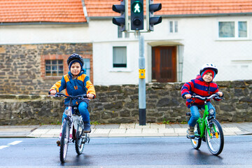 Two active kids boys in helmet biking on bicycles in the city. Happy children in colorful clothes and waiting for green traffic light. Safety and protection for preschool kids