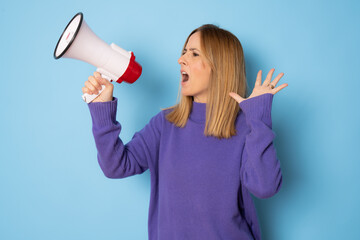 Young caucasian woman holding megaphone and screaming isolated over blue background.