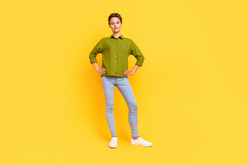 Fototapeta na wymiar Photo of confident successful lady hands hips posing wear green shirt jeans footwear isolated yellow color background