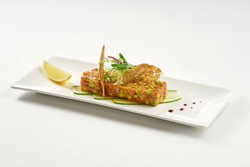 Appetizing salmon tartare with avocado in a white plate on a tablecloth