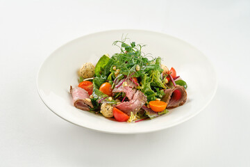 Salad with roast beef and pine nuts in a white plate.