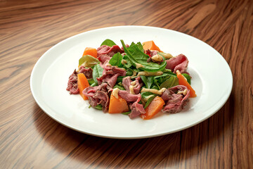 Salad with roast beef and pumpkin in a white plate.