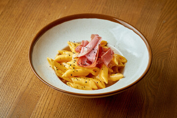 Cheese pasta with prosciutto in a plate on a wooden background