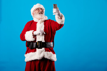 Fototapeta na wymiar Santa Claus taking a selfie with a mobile phone on a blue background
