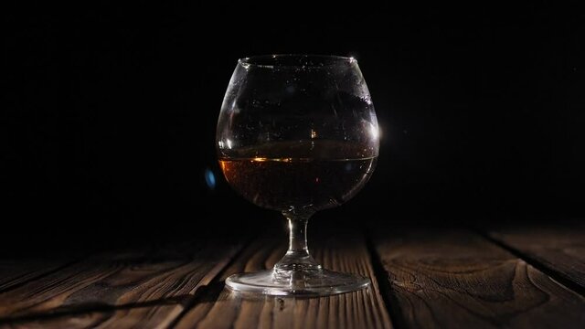Close-up cognac slowly rotates in a glass on a wooden background in the dark. Vintage wooden background in pub or bar. Cognac poured into a glass on a wooden background.