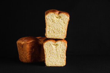 Brioche bread, cut in half, one part upon another, black background, dark and moody