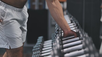 Arab man athlete is grabbing a dumbbell from a big selection in a fitness center.