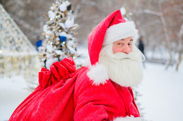 Portrait of an elderly man dressed as santa claus on the background of a christmas tree outdoors.