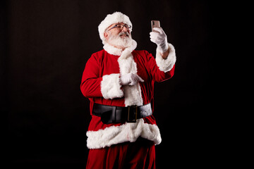 Fototapeta na wymiar Santa Claus taking a selfie with a mobile phone on a black background
