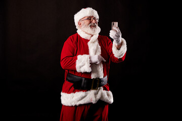 Fototapeta na wymiar Santa Claus taking a selfie with a mobile phone on a black background