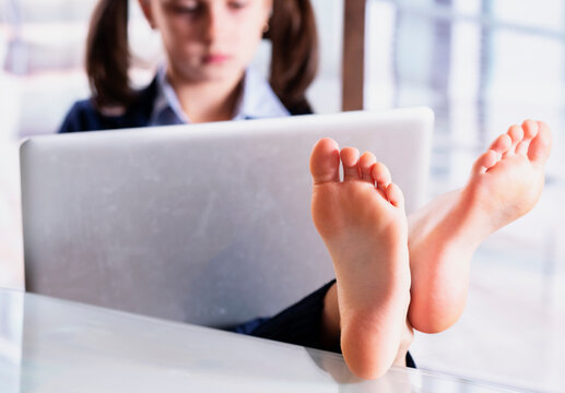 Humorous image of beautiful young business girl working in office with bare feet on desk. Selective focus on feet.