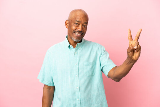 Cuban senior isolated on pink background smiling and showing victory sign