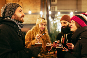 Happy smiling friends with cups of mulled wine having fun, spending time together at winter fair at evening. Holidays, Christmas concept