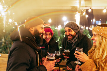 Young happy people, friends with glasses of beer and sausages laughing, spending time together at winter fair at evening. Holidays, Christmas concept
