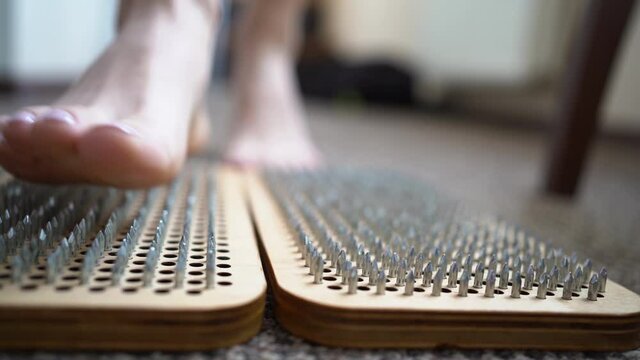 Female bare feet standing on a wooden sadhu board with sharp nails, bottom view. Foot acupuncture massage. Woman practicing yoga relaxation.
