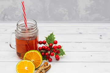 Black hot tea in a glass jar, lemon, cinnamon and holly on a white wooden background. New year and...