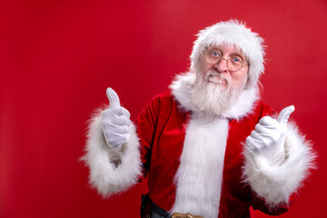 Portrait Santa Claus in Christmas hat red suit show gesture thumb up like, showing thumb up Finger up. Like on red studio background.