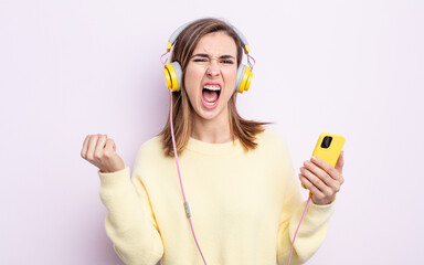 young pretty woman shouting aggressively with an angry expression. headphones and phone concept