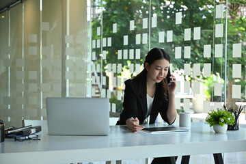 Photo of a businesswoman talking on mobile phone while using a digital tablet and stylus pen at the...