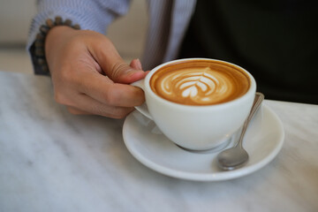 Closeup image of a young smart man holding a coffee cup with latte art in the comfortable living room.