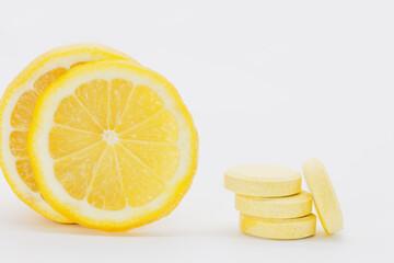 Vitamin "C" tablets on a white background. In the background, a sliced ​​lemon.