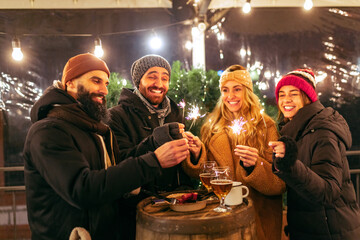 Happy smiling friends with cups of mulled wine having fun, spending time together at winter fair at evening. Holidays, Christmas concept