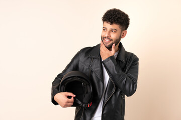 Young Moroccan man with a motorcycle helmet isolated on beige background looking up while smiling