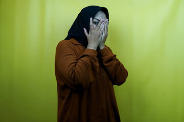 Beautiful young asian muslim woman with eyes peeking between fingers, isolated