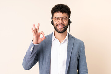 Telemarketer Moroccan man working with a headset isolated on beige background showing ok sign with fingers