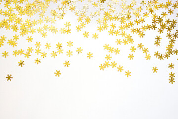 Golden confetti in the form of snowflakes on white background. Festive day backdrop. Flat lay style with minimalistic design. Template for banner or party invitation