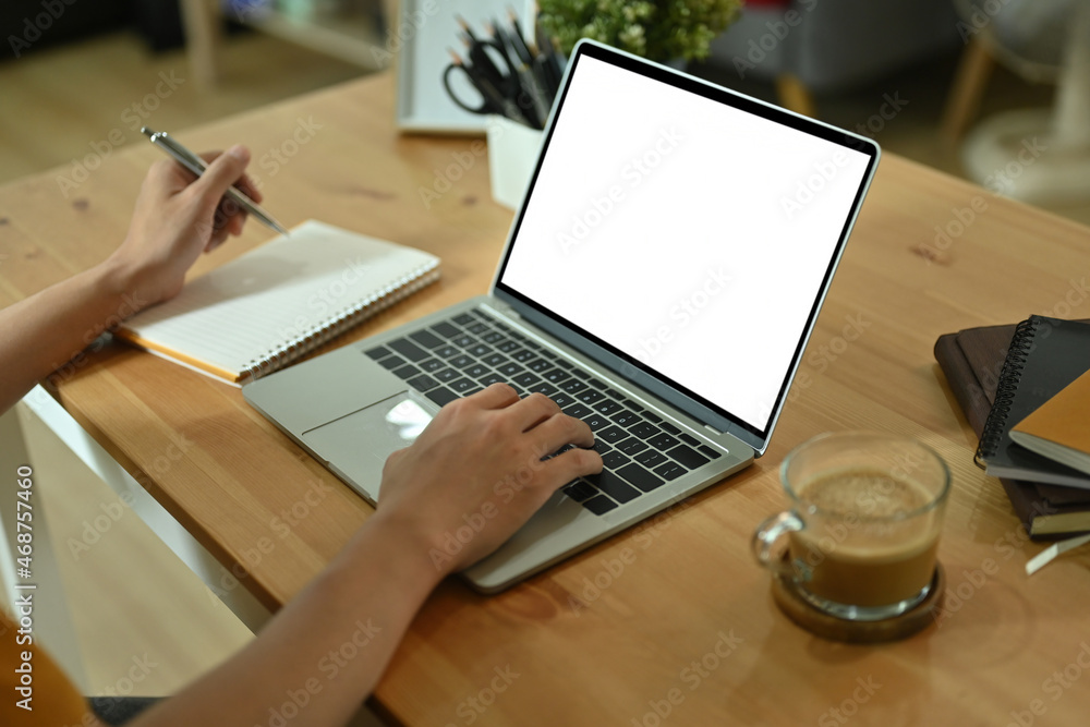 Poster cropped image of a hand taking notes at the wooden table surrounded by a computer laptop, stack of b