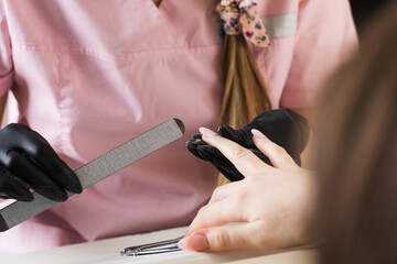  A manicurist files nails with a metal file. Manicure process in a beauty salon.