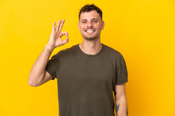 Young caucasian handsome man isolated on yellow background showing ok sign with fingers