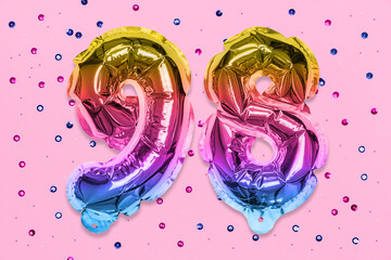 Rainbow foil balloon number, digit ninety eight on a pink background with sequins. Birthday...