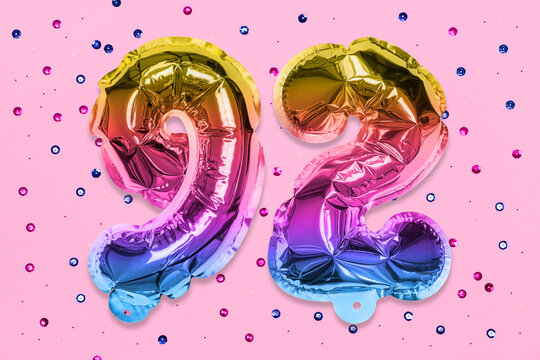 Rainbow foil balloon number, digit ninety two on a pink background with sequins. Birthday greeting card with inscription 92. Top view. Numerical digit. Celebration event, template.
