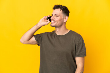 Fototapeta premium Young caucasian handsome man isolated on yellow background keeping a conversation with the mobile phone