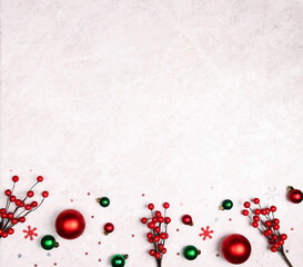 Christmas border of red and green decorations and berries on light marble background.