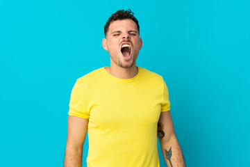 Young caucasian handsome man isolated on blue background shouting to the front with mouth wide open