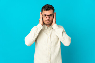 Young caucasian handsome man isolated on blue background frustrated and covering ears