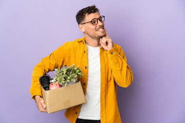 Young caucasian man making a move while picking up a box full of things isolated on purple...