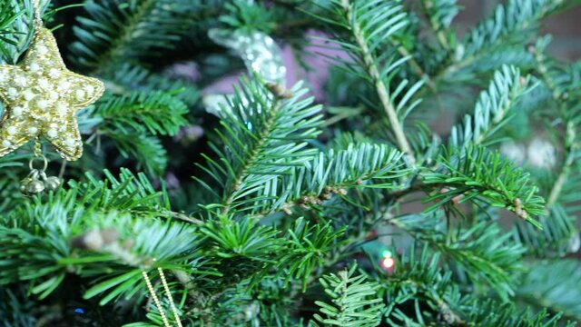 A closeup panning shot of a purple, mauve, beaded, Christmas ornament with minature moon and star gently moving while hanging in an evergreen tree